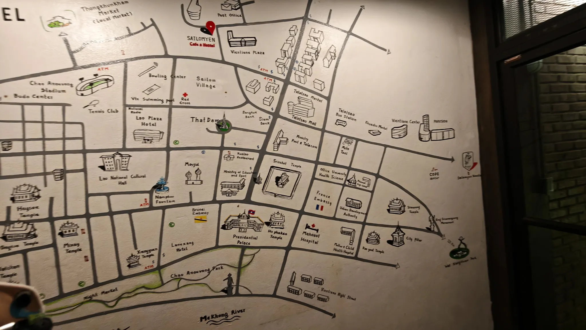 Hand-drawn illustrated map of Vientiane city on a hostel wall showing landmarks, temples and the Mekong River