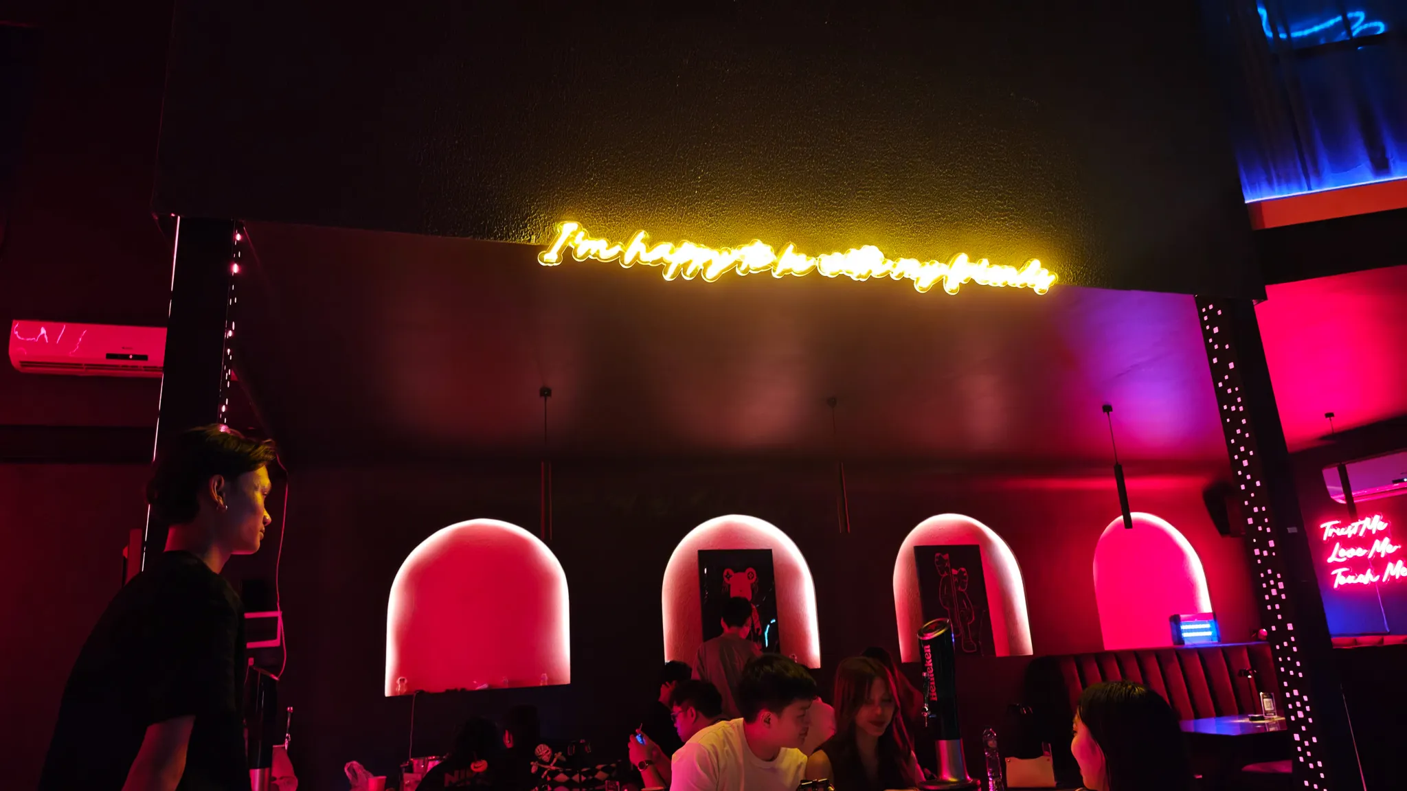 Stylish Vientiane bar interior with neon script sign, pink-lit arched alcoves and moody lighting