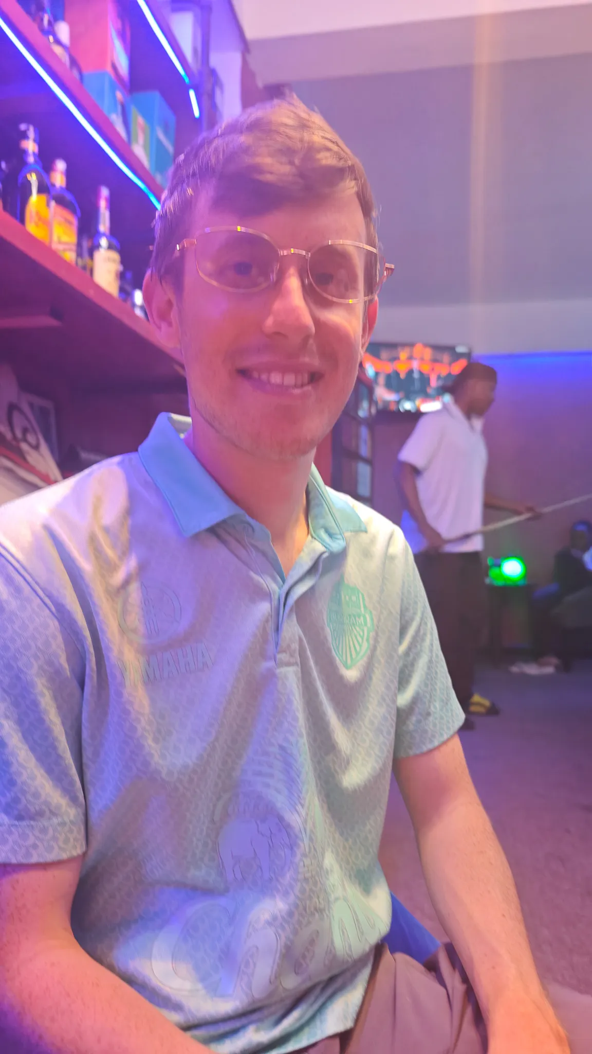 Portrait at a bar in Vientiane wearing glasses with neon-lit shelves of spirits in the background