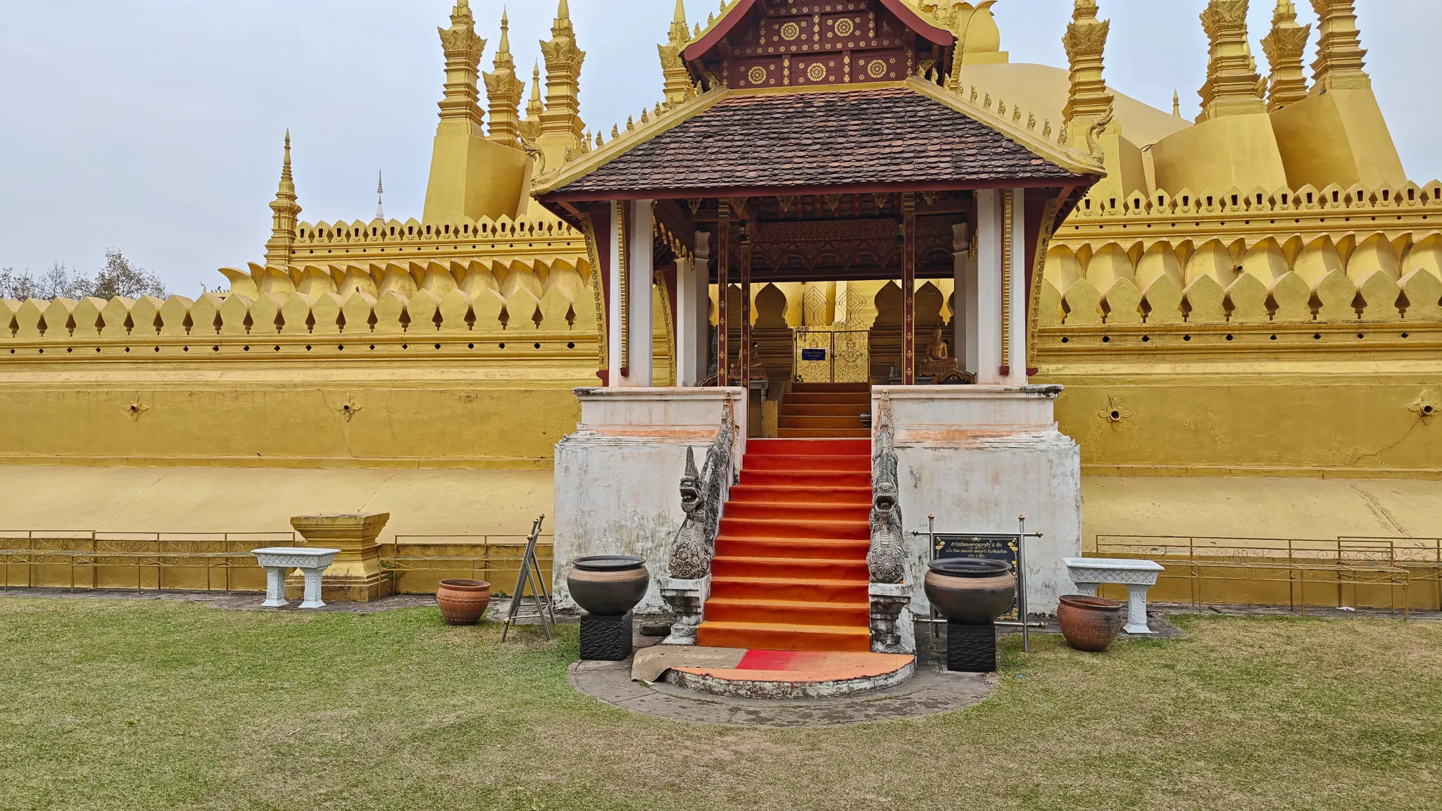 Red-carpeted entrance stairway with naga guardians leading into Pha That Luang golden stupa in Vientiane