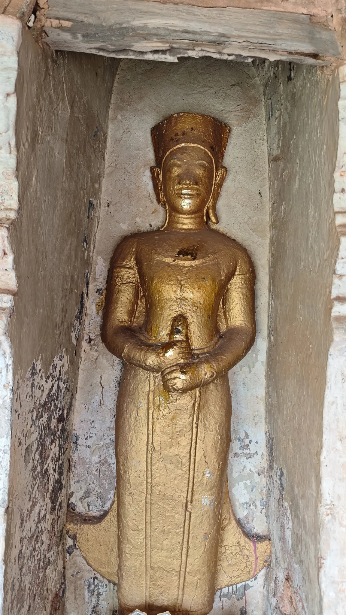 Small golden Buddha statue in a niche of the Pha That Luang stupa wall in Vientiane