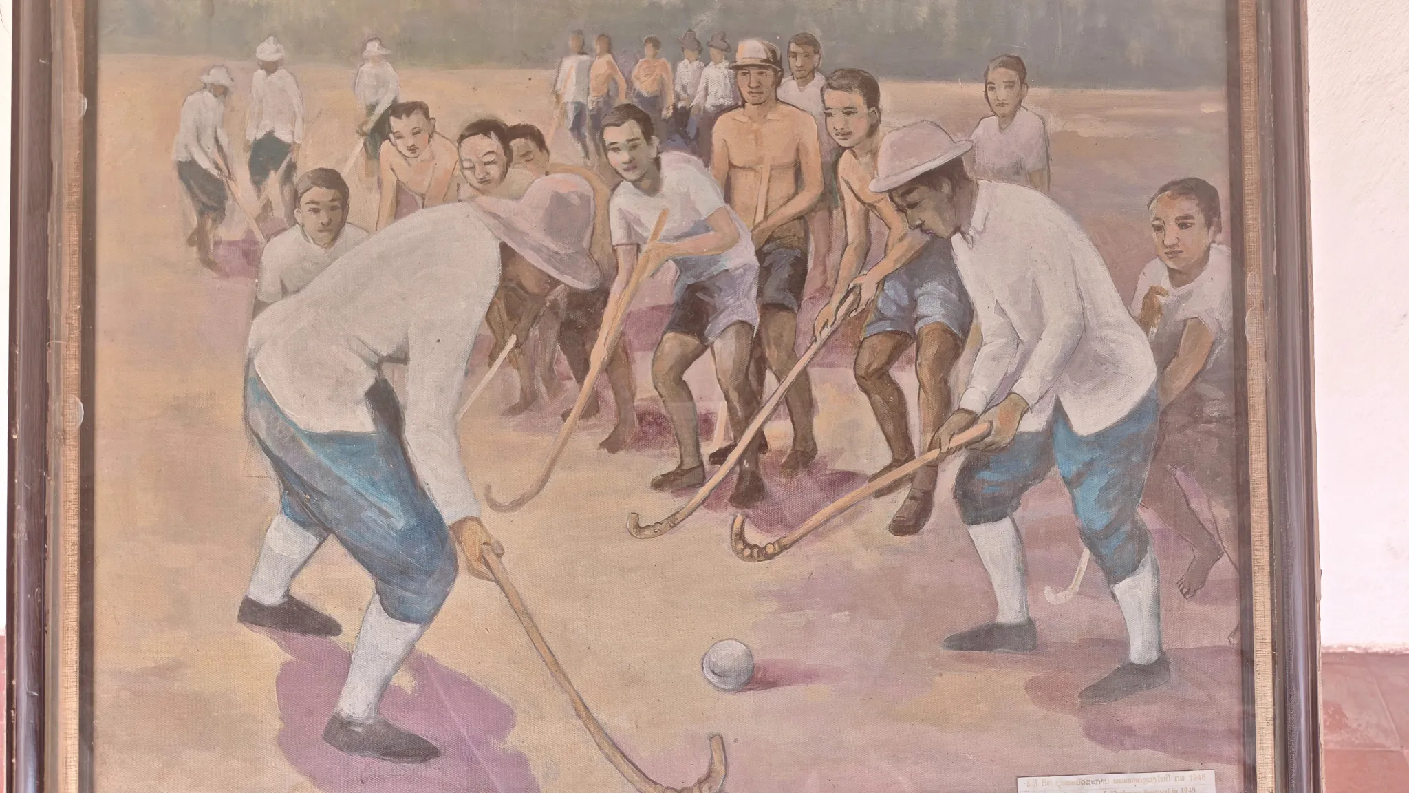 Historical painting of Lao men playing field hockey displayed inside the Pha That Luang temple complex in Vientiane