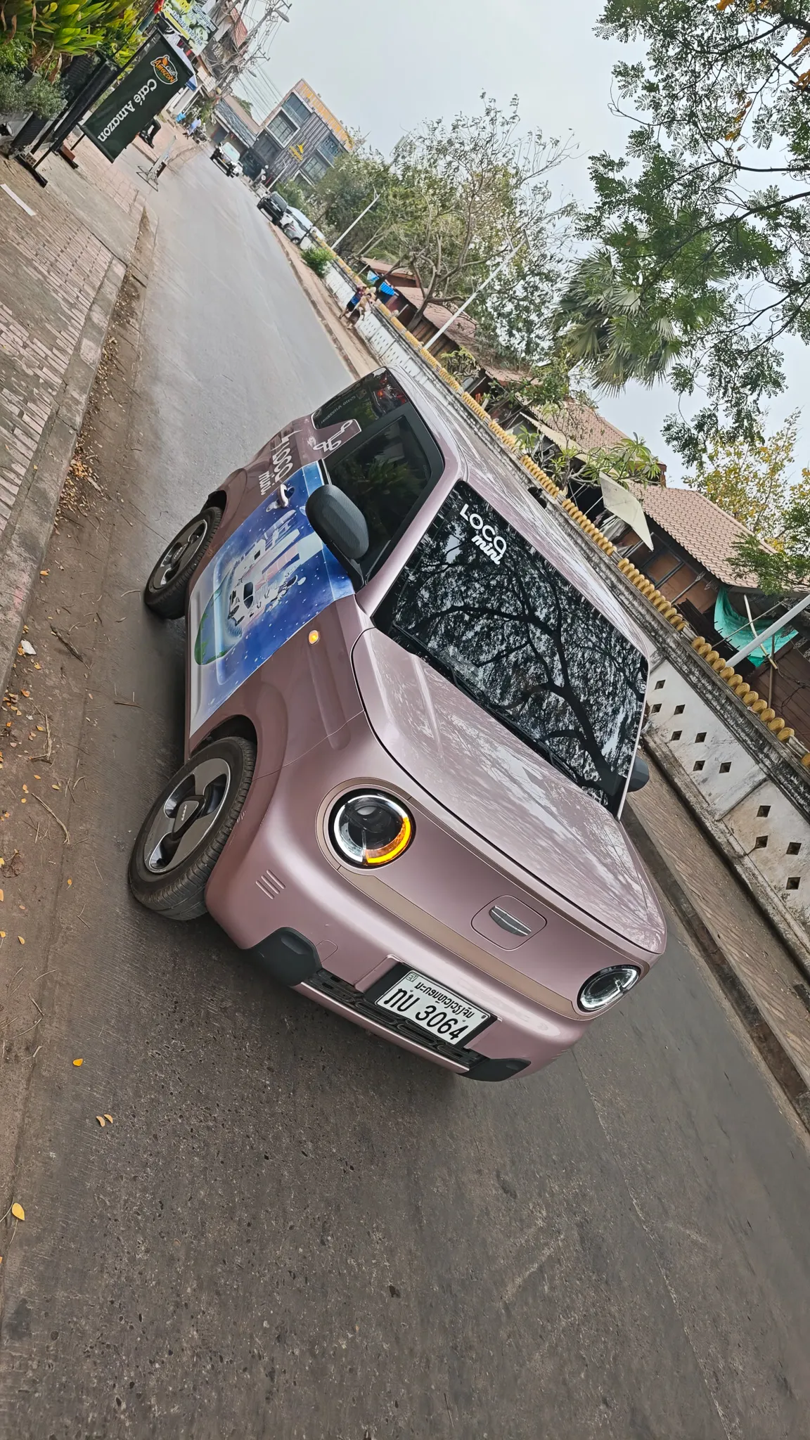 Pink Loco brand electric mini car parked on a Vientiane street with temples and cafes nearby