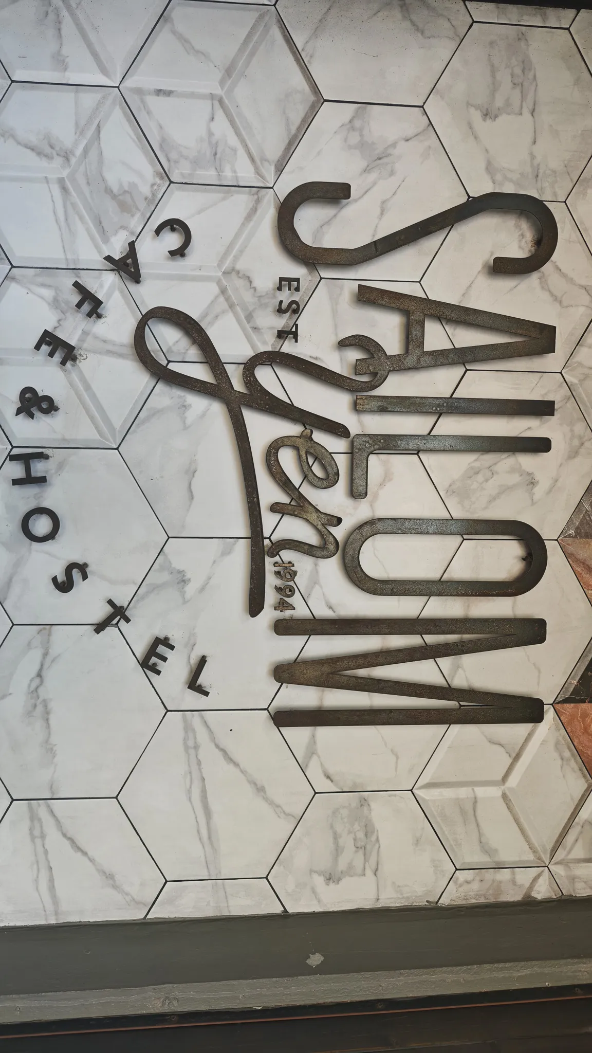 Metal letter sign reading Salon Est 1994 Cafe and Hostel on a marble hexagonal tile wall in Vientiane