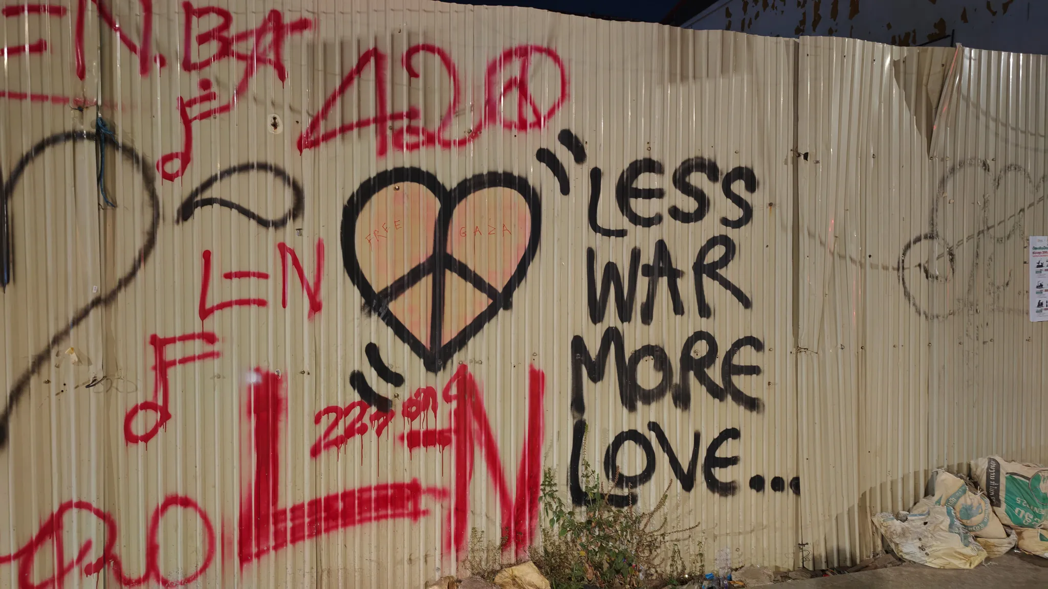 Street art graffiti reading Less War More Love with a peace sign heart on corrugated metal in Vientiane