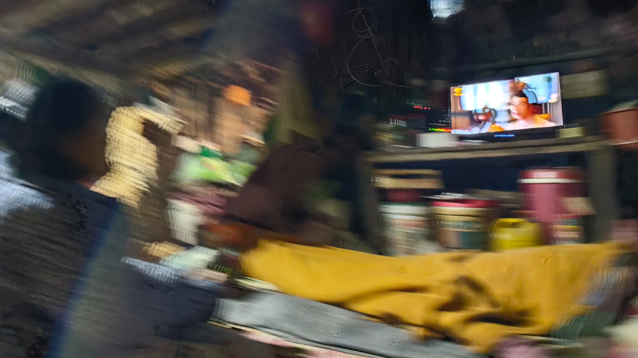 Blurry interior of a village house at night with a TV screen glowing among household items in Ban Haddean, Laos