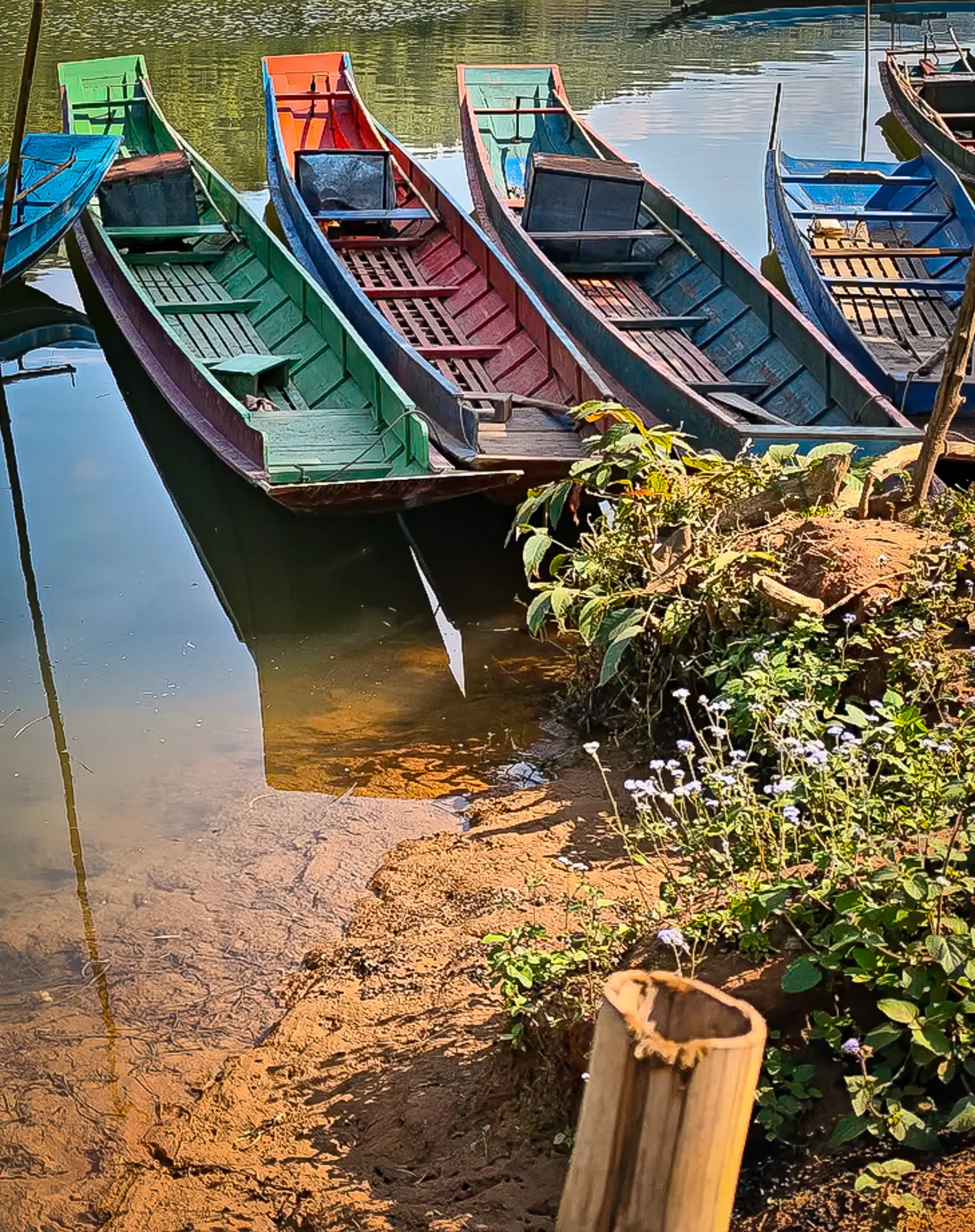 Two village houses with red roofs perched on an eroded riverbank with a blue longboat moored on the Nam Ou river in Laos