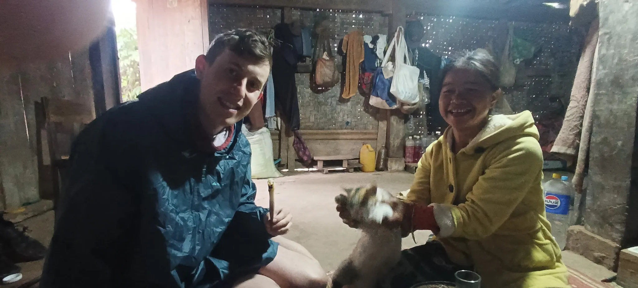 Traveller and local villager host with a cat inside a traditional hut during morning breakfast along the Nam Ou river in Laos